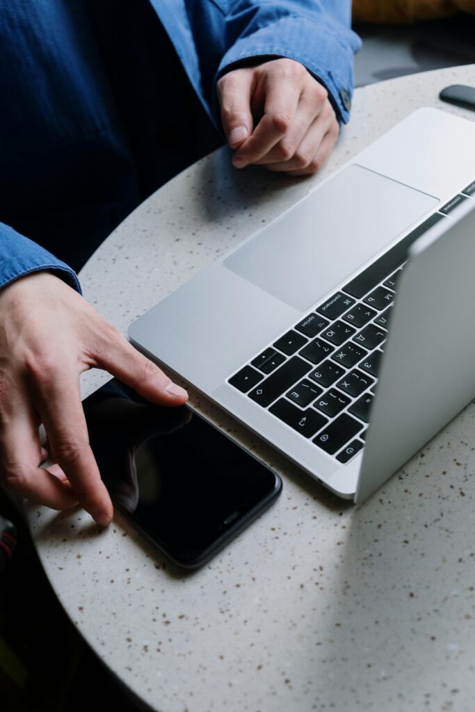 A close-up of hands exchanging phone next to a laptop on a round table.